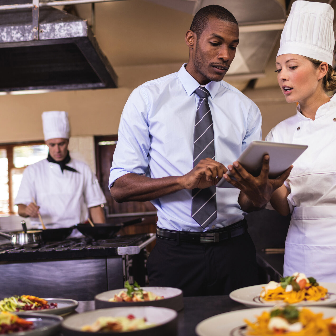 Male manager and female chef using digital tablet in kitchen at hotel